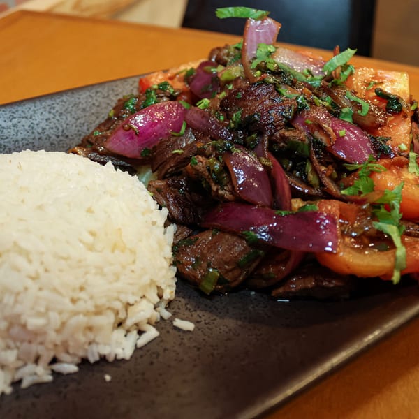 Venezuelan Lomo Saltado with beef, red onions, tomatoes, cilantro, and white rice on a dark plate.