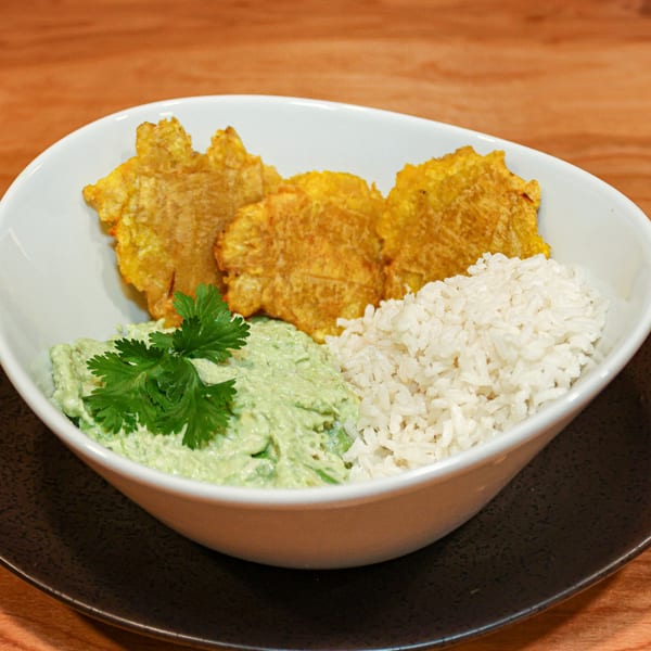 Venezuelan dish with fried plantains, white rice, and green avocado sauce topped with cilantro.