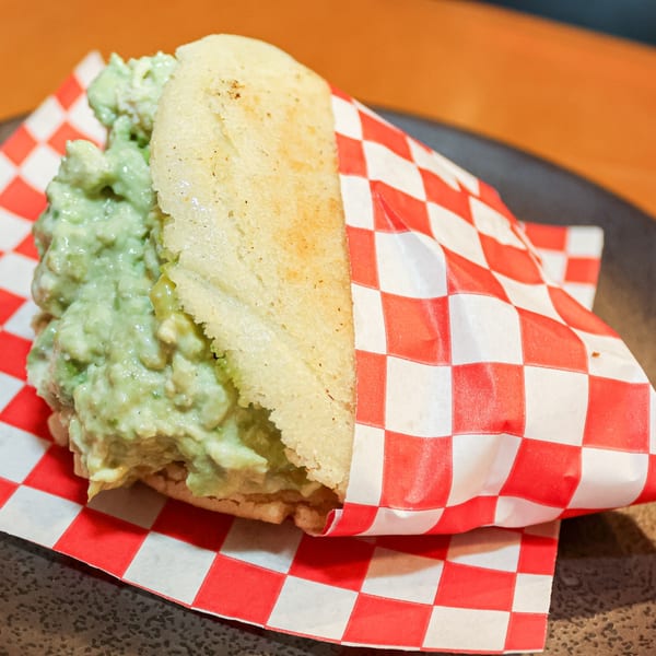 Avila Restaurant's Venezuelan arepa, filled with green avocado chicken salad, wrapped in red and white checkered paper.