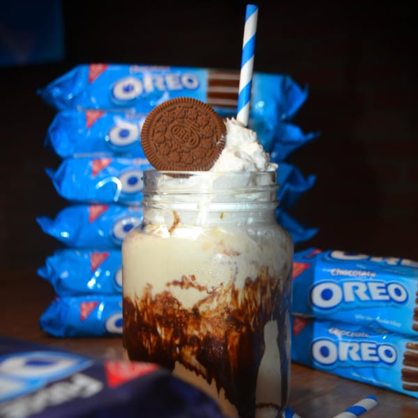 Oreo milkshake in a mason jar with whipped cream, an Oreo cookie, and a blue-striped straw.