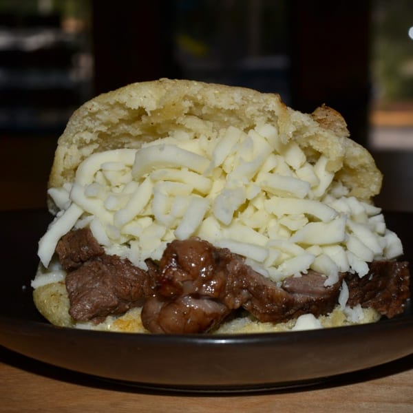 A Venezuelan arepa from Avila Restaurant, filled with shredded beef and white cheese, on a dark plate.