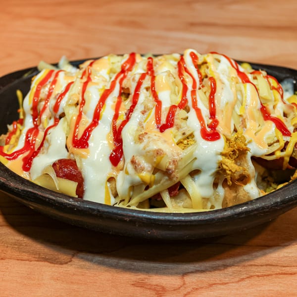 Venezuelan dish with fries, shredded chicken, cheese, ketchup, and white and yellow sauces.