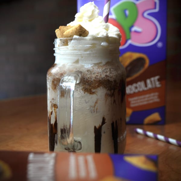 A chocolate milkshake in a mason jar with whipped cream, cookies, and a striped straw.