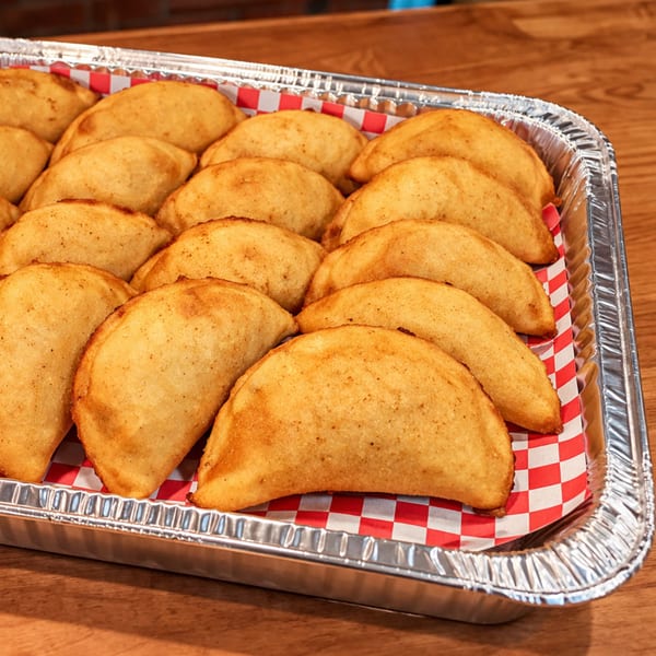 A catering tray filled with golden-brown Venezuelan empanadas on red and white checkered paper.