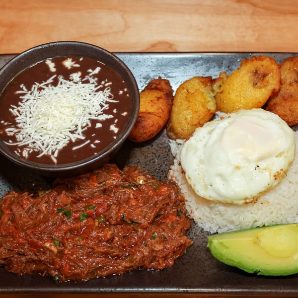 Venezuelan dish with shredded beef, rice, black beans with cheese, fried plantains, fried egg, and avocado.