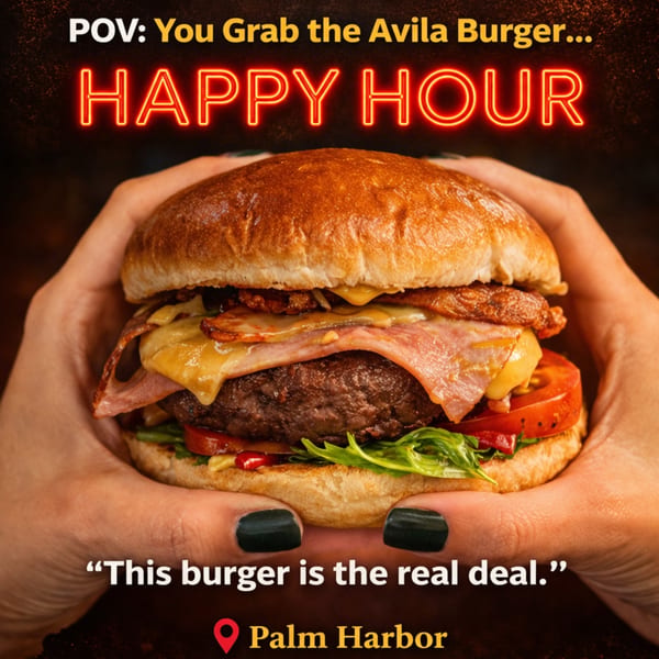 Hands holding a large Avila burger with melted cheese, bacon, ham, tomato, and lettuce.