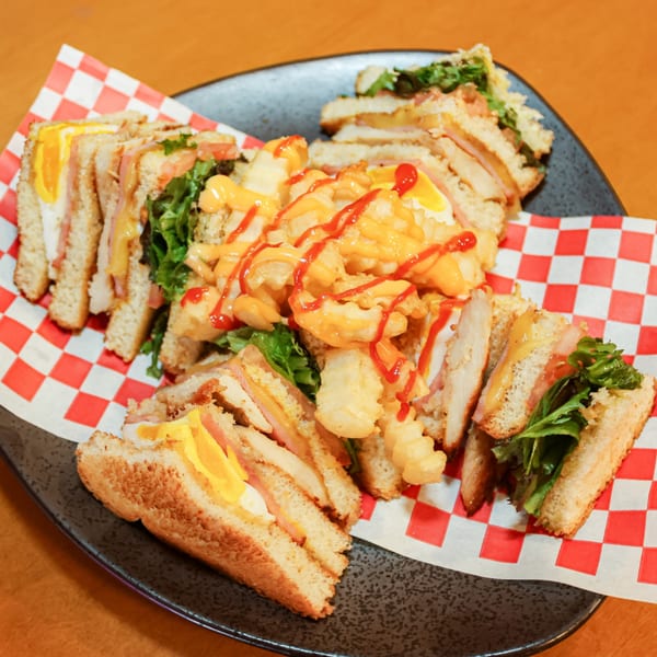 Club sandwiches with ham, cheese, egg, and lettuce, served with waffle fries drizzled with sauces.