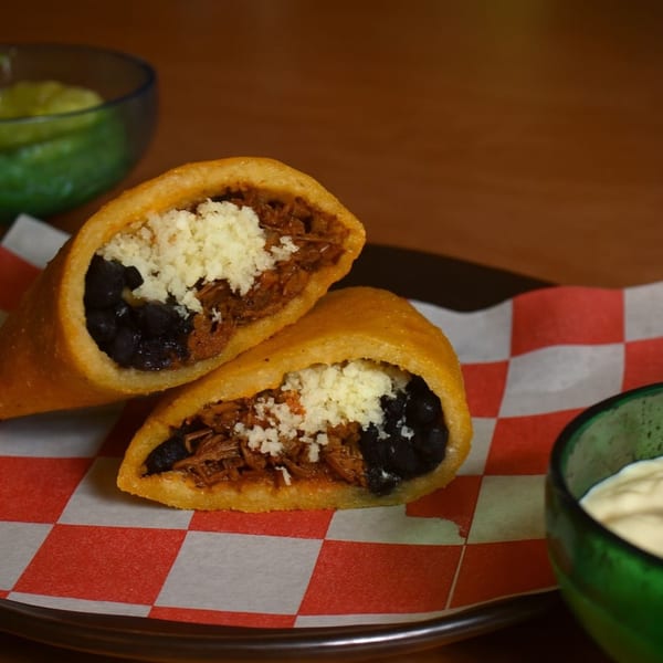Two Venezuelan empanadas, one cut open, filled with shredded beef, black beans, and white cheese.