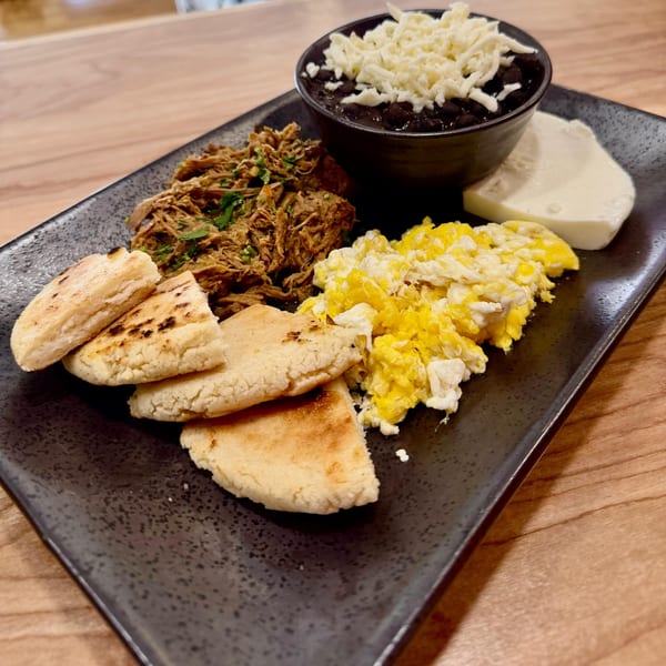 Venezuelan breakfast with shredded beef, scrambled eggs, black beans, cheese, and arepas on a black plate.