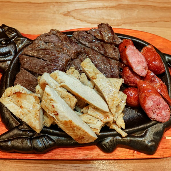 Sizzling platter of Venezuelan grilled steak, chicken, and sausages on a wooden board.