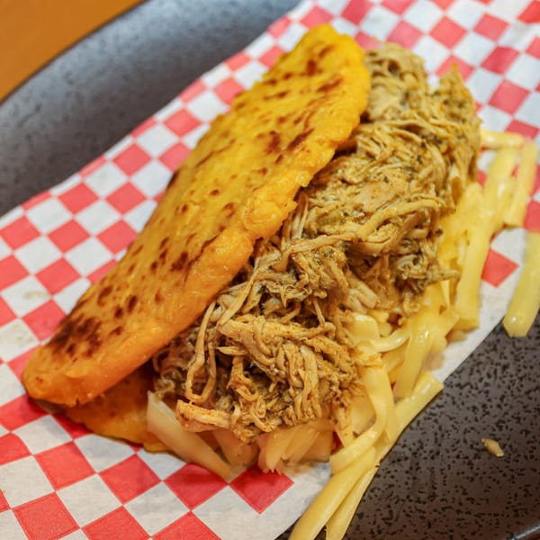 A Venezuelan arepa from Avila Restaurant, filled with shredded chicken and cheese, on checkered paper.